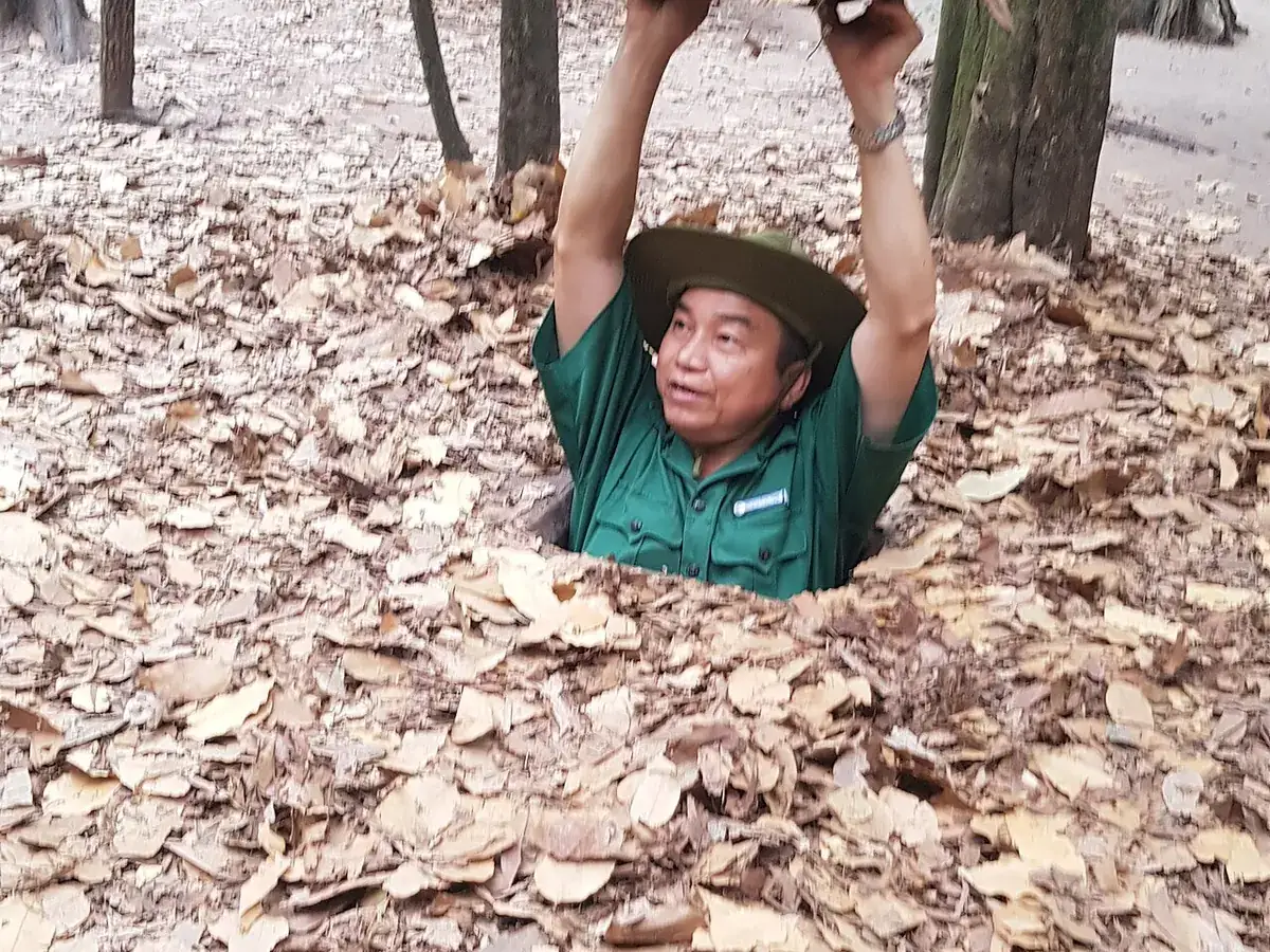 A person climbing out of a narrow Cu Chi tunnel entrance